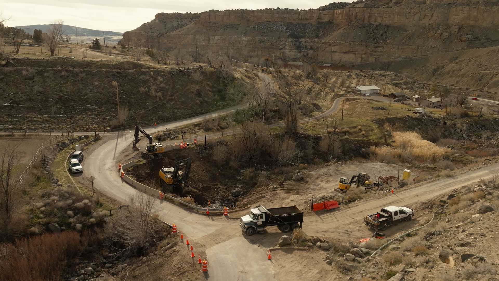 Wide dirt road in a barren quarry with several pickup trucks and heavy machinery under overcast skies