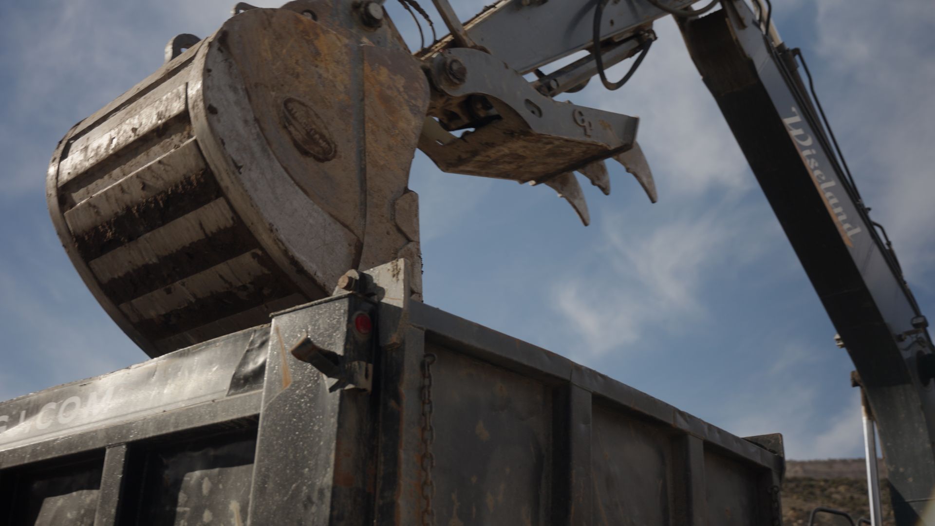 Excavator bucket dumping rubble into a large dumpster under a cloudy sky