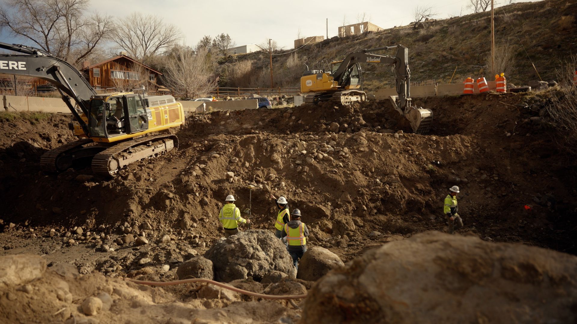 Construction workers excavating a large dirt pit with heavy machinery at a roadwork site