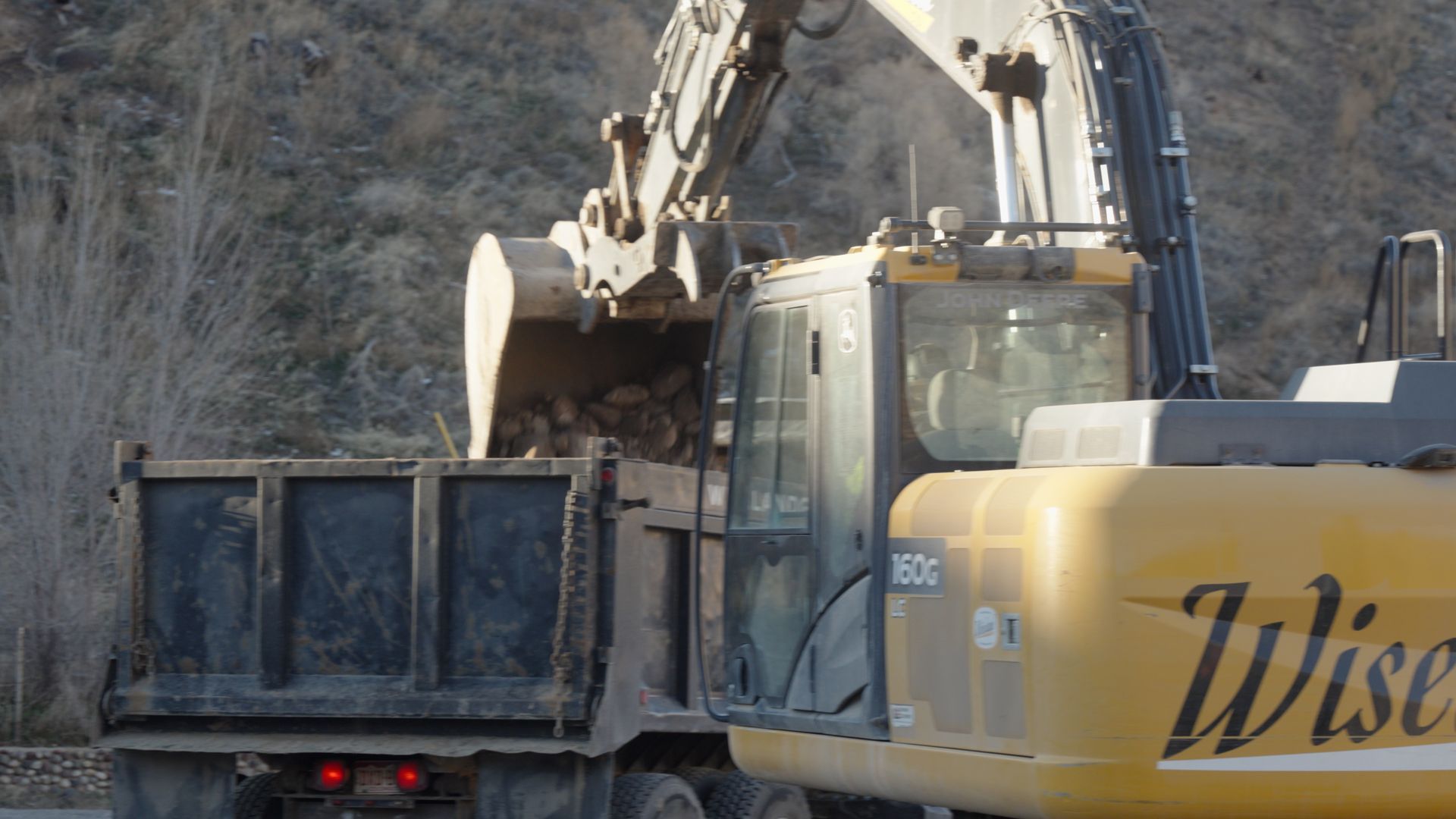 Excavator loading dirt into a dump truck at a rocky construction site.