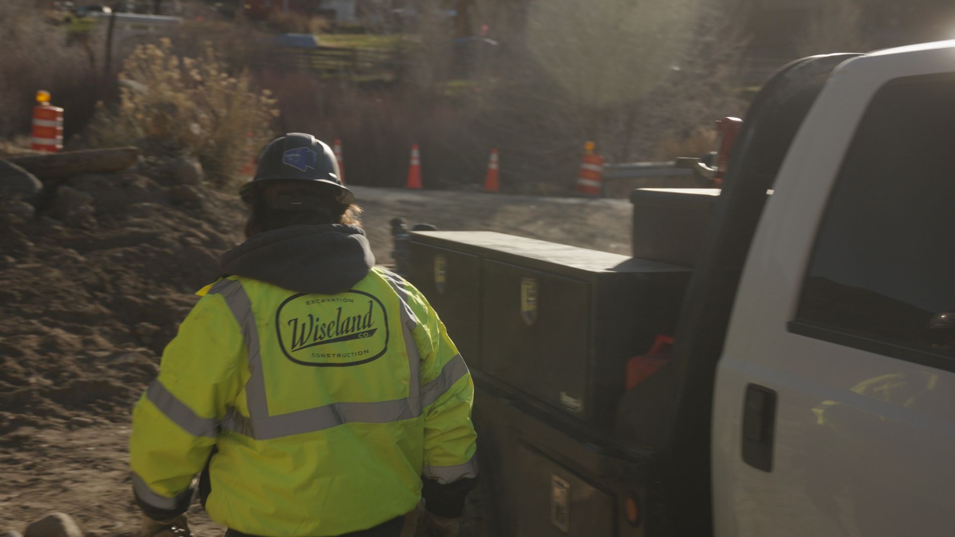 Worker in a neon yellow safety jacket stands beside a truck at a roadwork site.