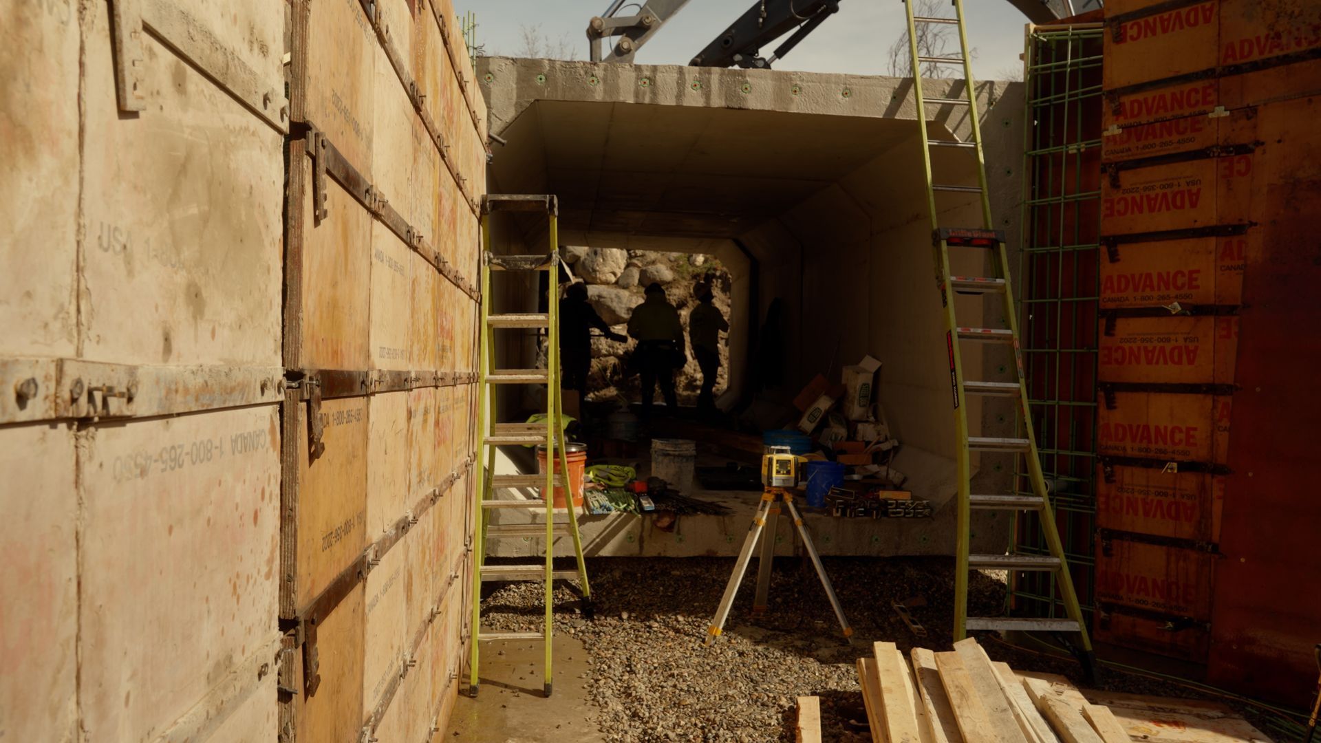 Construction site with concrete walls, ladders, tools, and workers in a tunnel-like opening