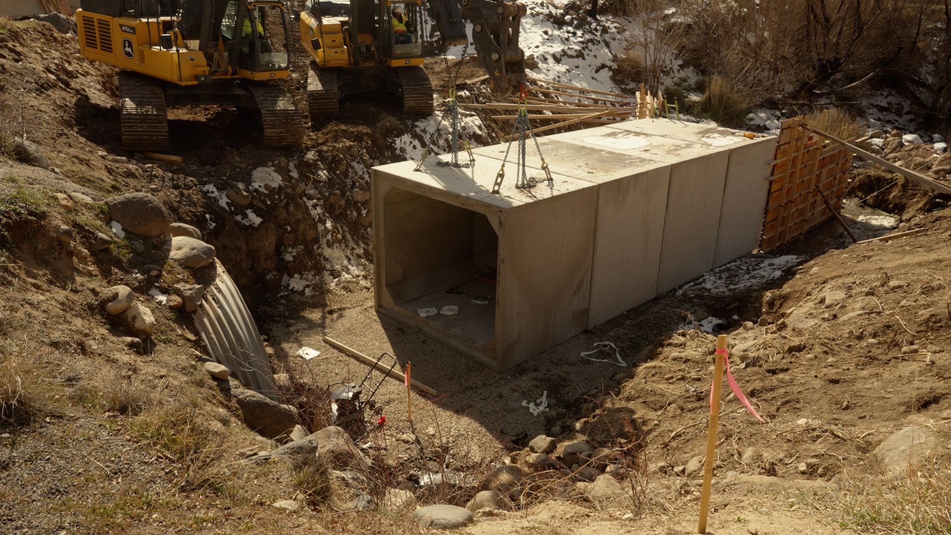 Concrete storm drain culvert at a rocky construction site with excavator in the background