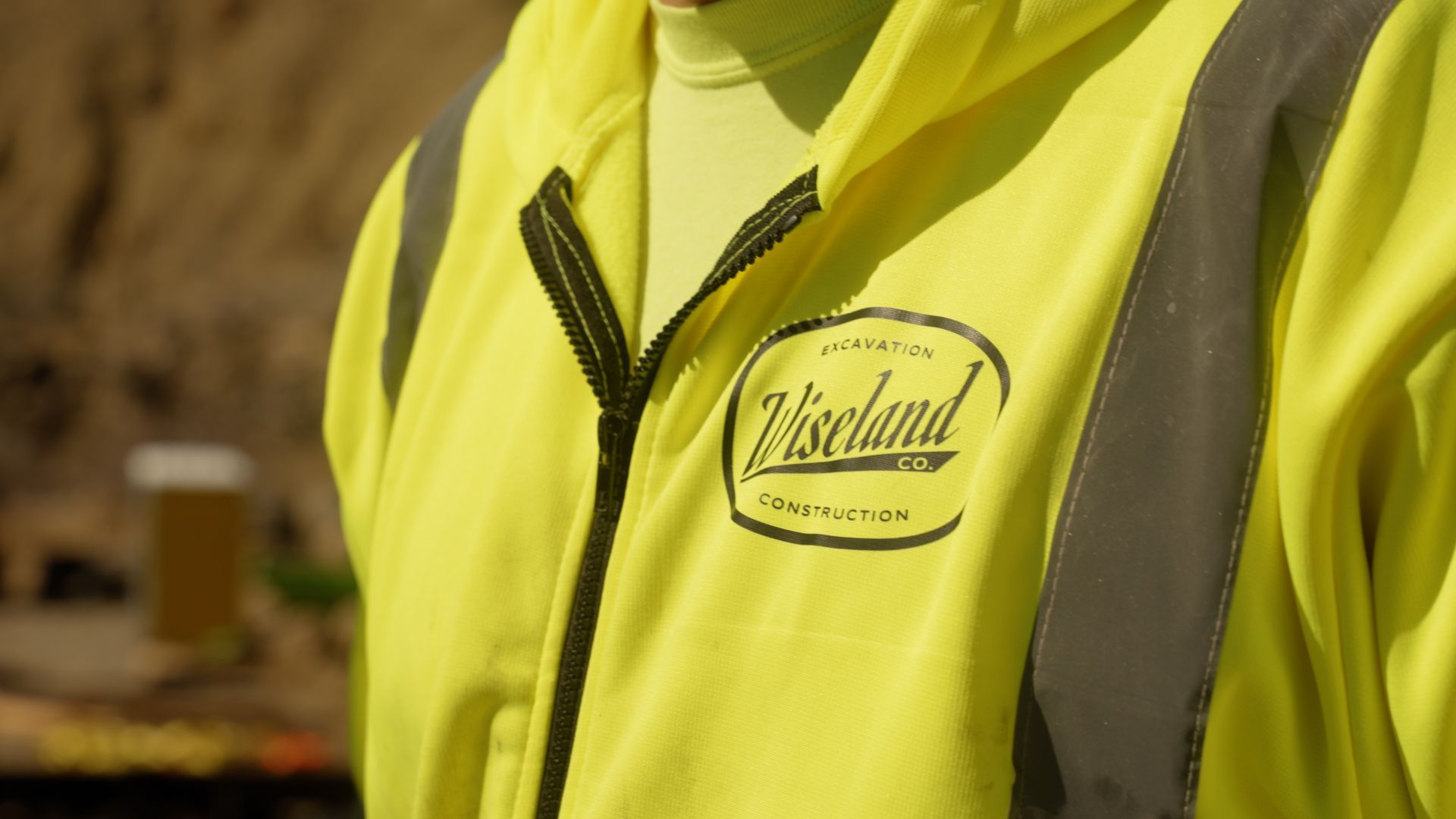Person in a neon yellow Zikeland jacket with black zipper and gray trim outdoors