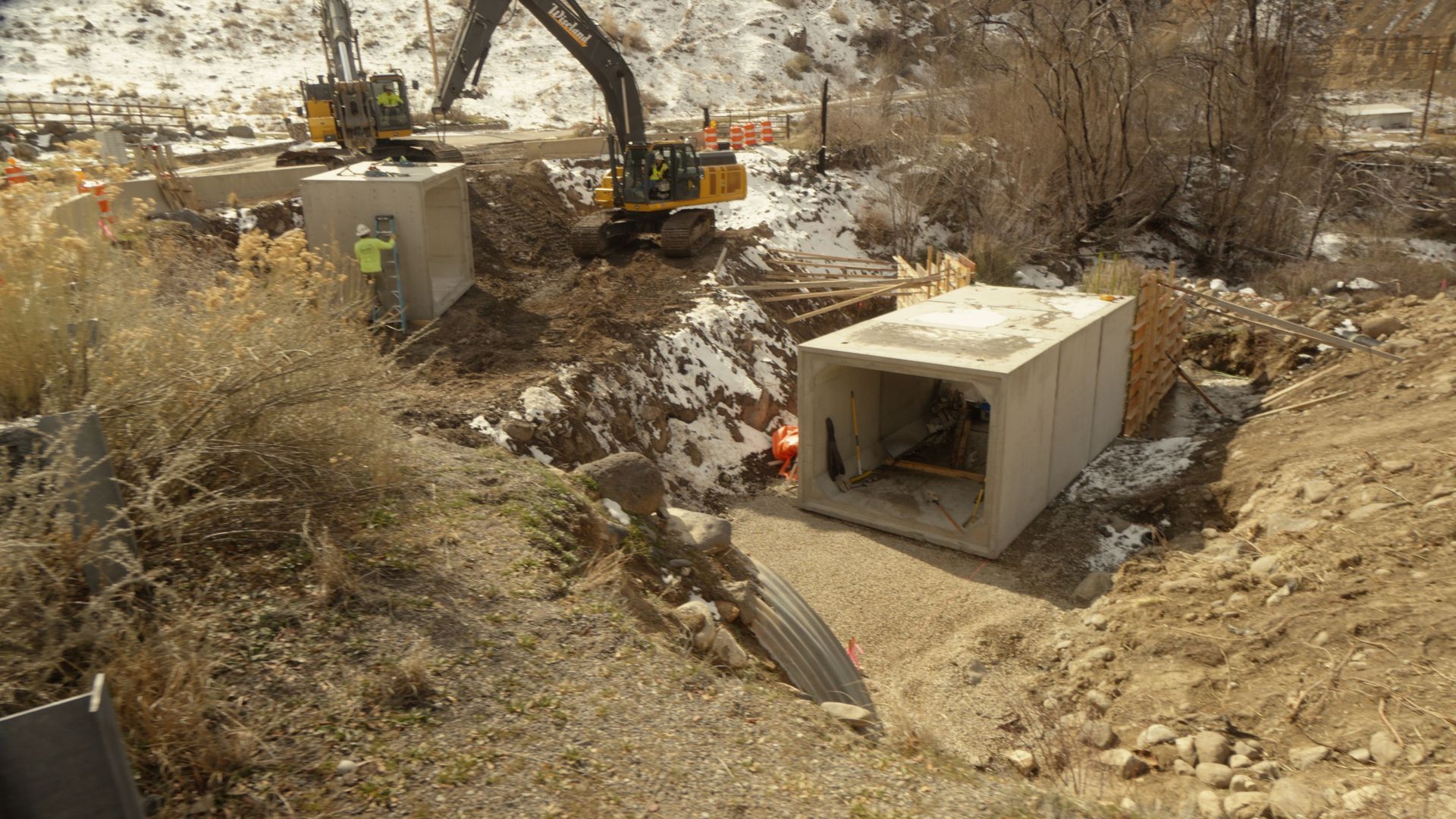 Excavator working in a dry construction site beside concrete culverts and exposed earth
