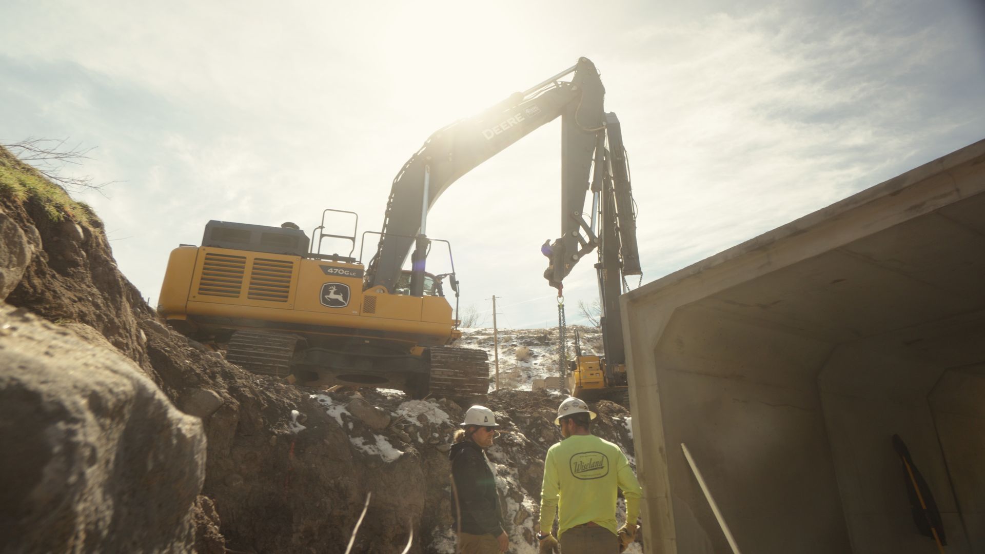 Yellow excavator lifting debris beside a concrete structure at a rocky construction site