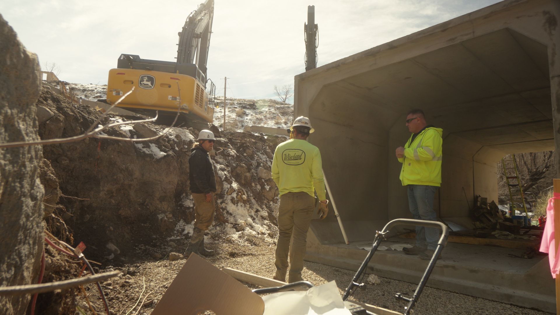 Construction workers near an excavator beside a collapsed concrete structure and debris