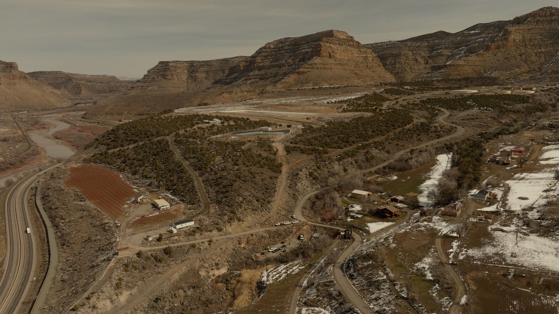 Rocky desert hills with winding roads and scattered buildings under a hazy sky