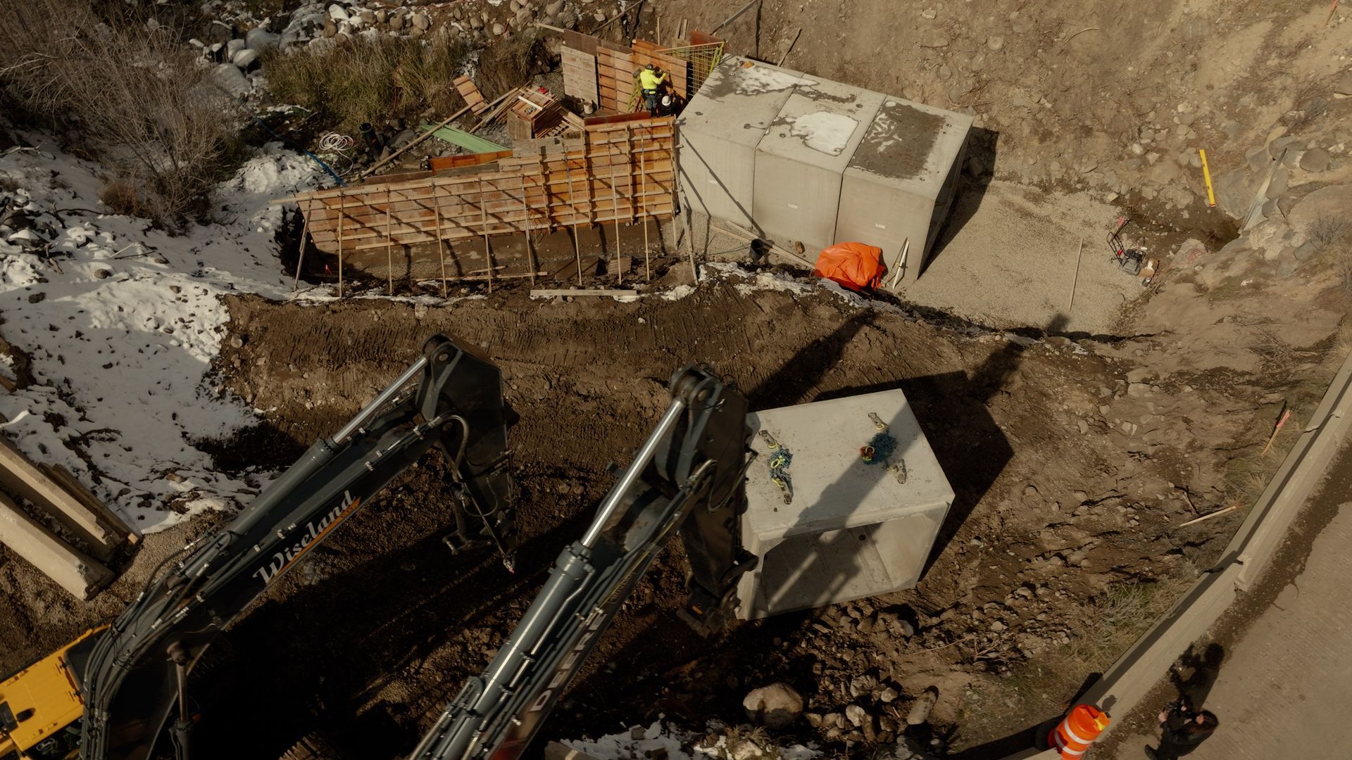 Excavator arms at a construction site beside a dirt trench and concrete barriers