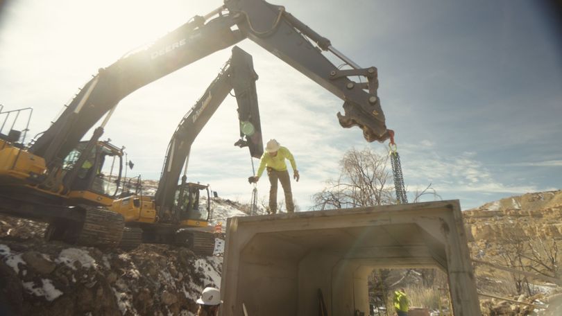 Construction worker standing beside a large excavator at a demolition site under bright daylight