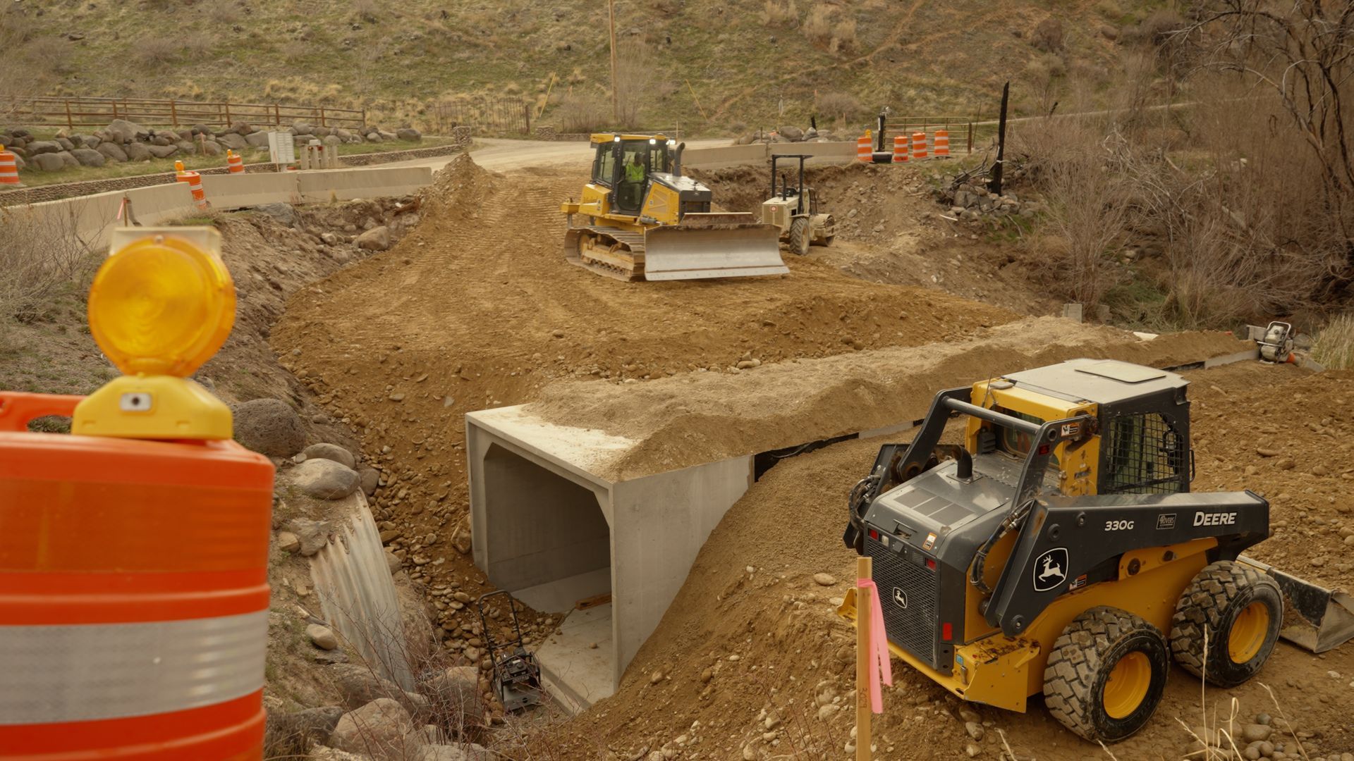 Construction site with excavators and a front loader building a concrete culvert in a dirt trench