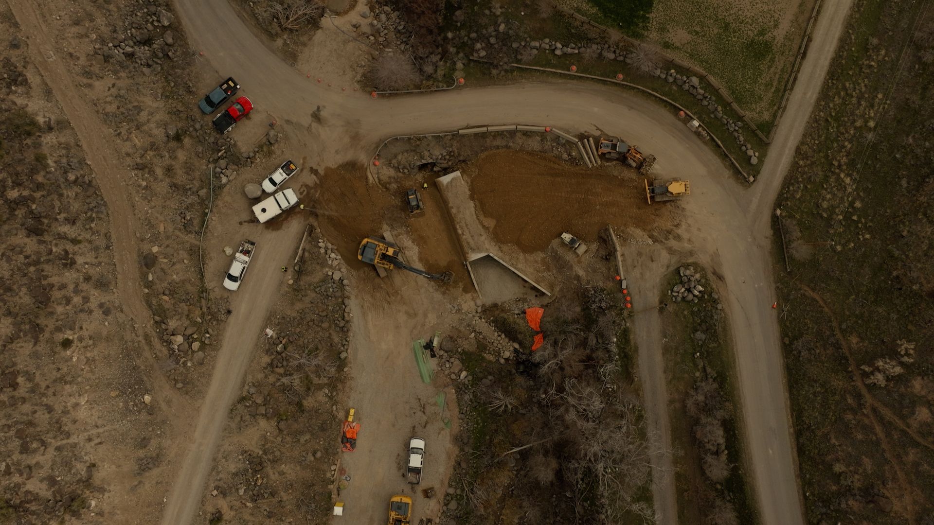 Aerial view of a construction site with heavy equipment, dirt roads, and a partially built circular structure.