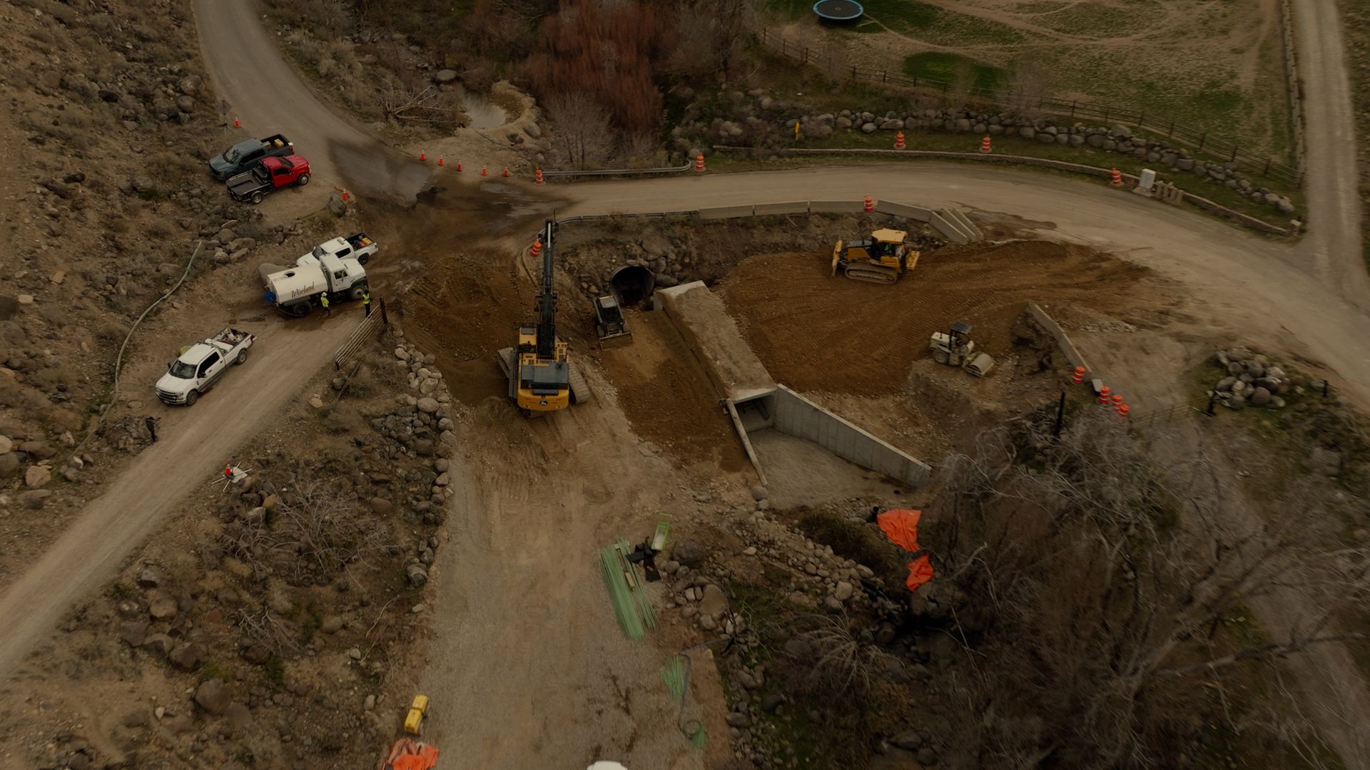 Aerial view of a road construction site with excavators, trucks, and dirt piles on a winding path