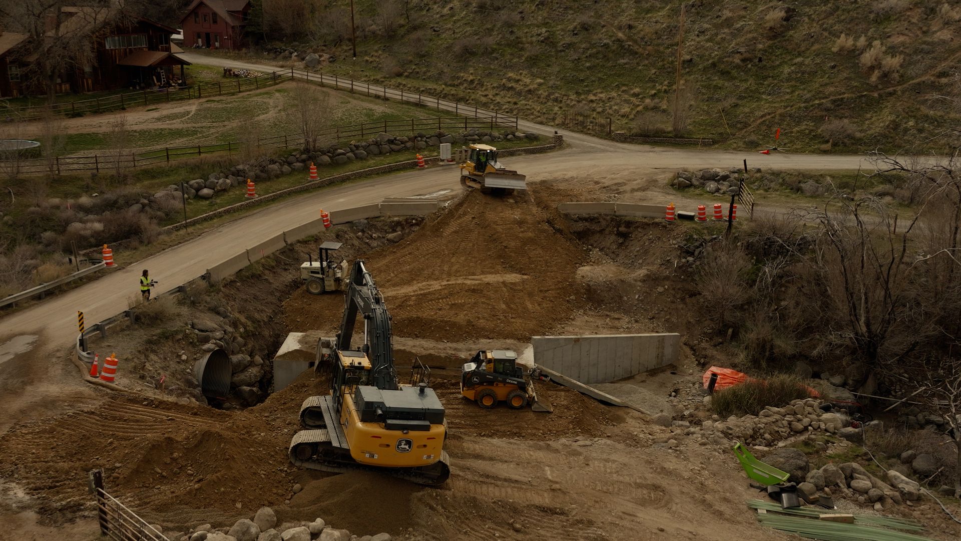 Construction site with excavators and trucks digging a large dirt embankment beside a winding road