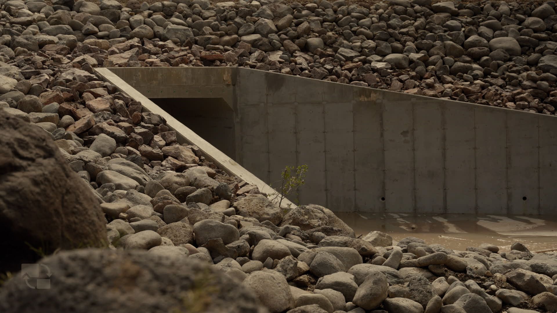 Rock-lined concrete drainage channel beneath a stone embankment barrier