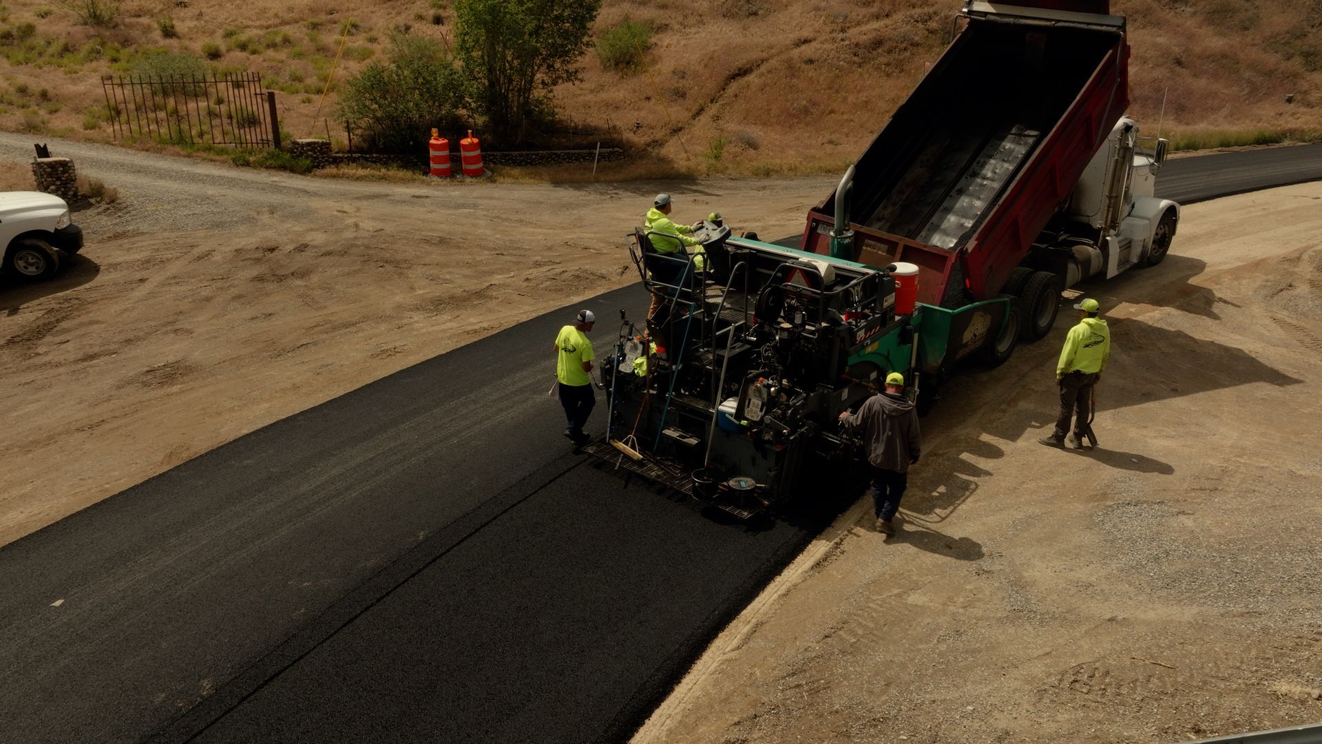 Road workers paving asphalt near a dump truck on a dirt construction site