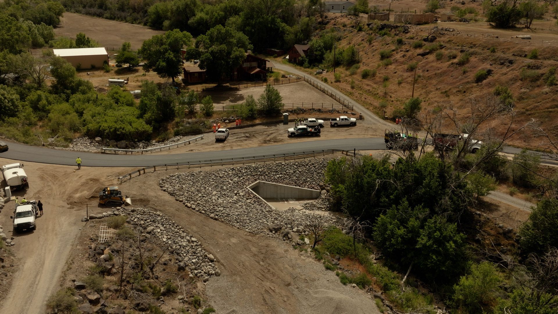 Winding road through a dry hillside with a few parked vehicles and scattered trees
