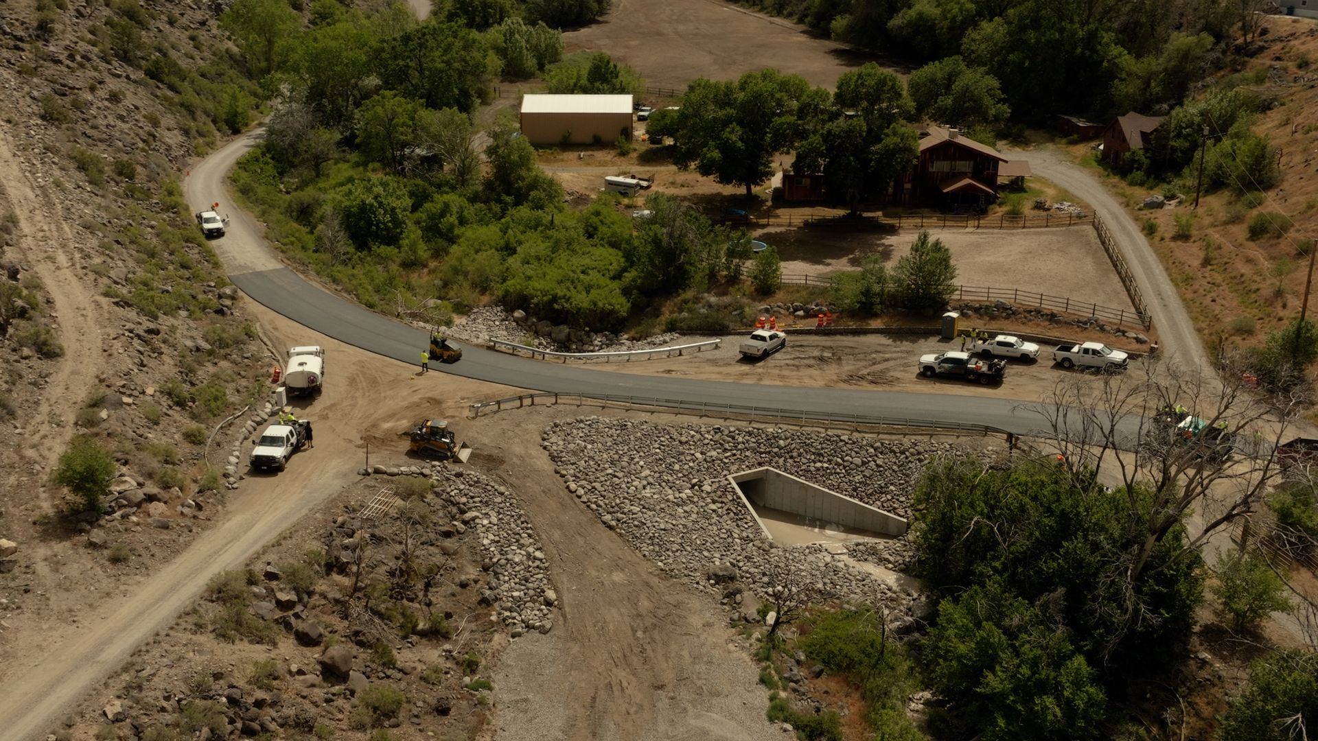 Aerial view of cars crossing a small bridge on a mountain road beside a rocky dry ravine