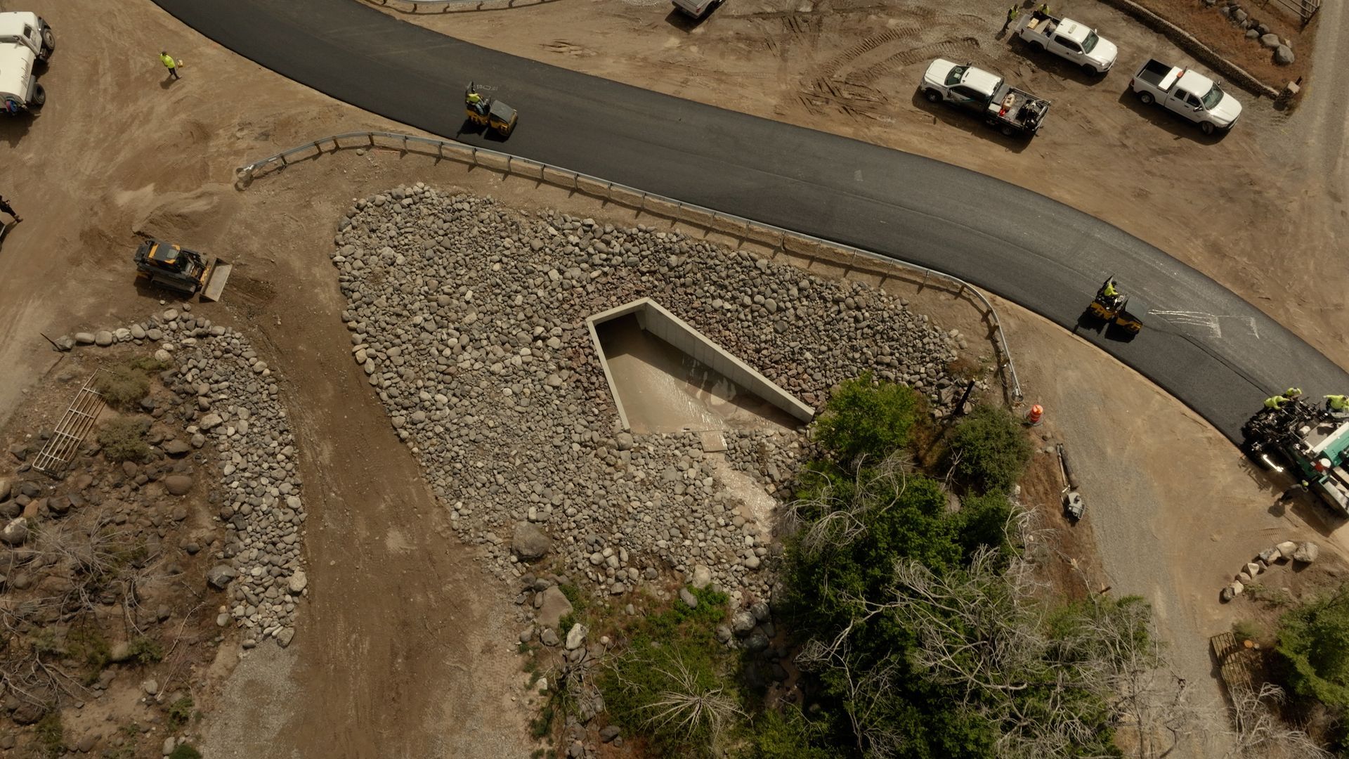 Aerial view of a stone-lined rectangular water feature beside a curved road in a dry landscape.