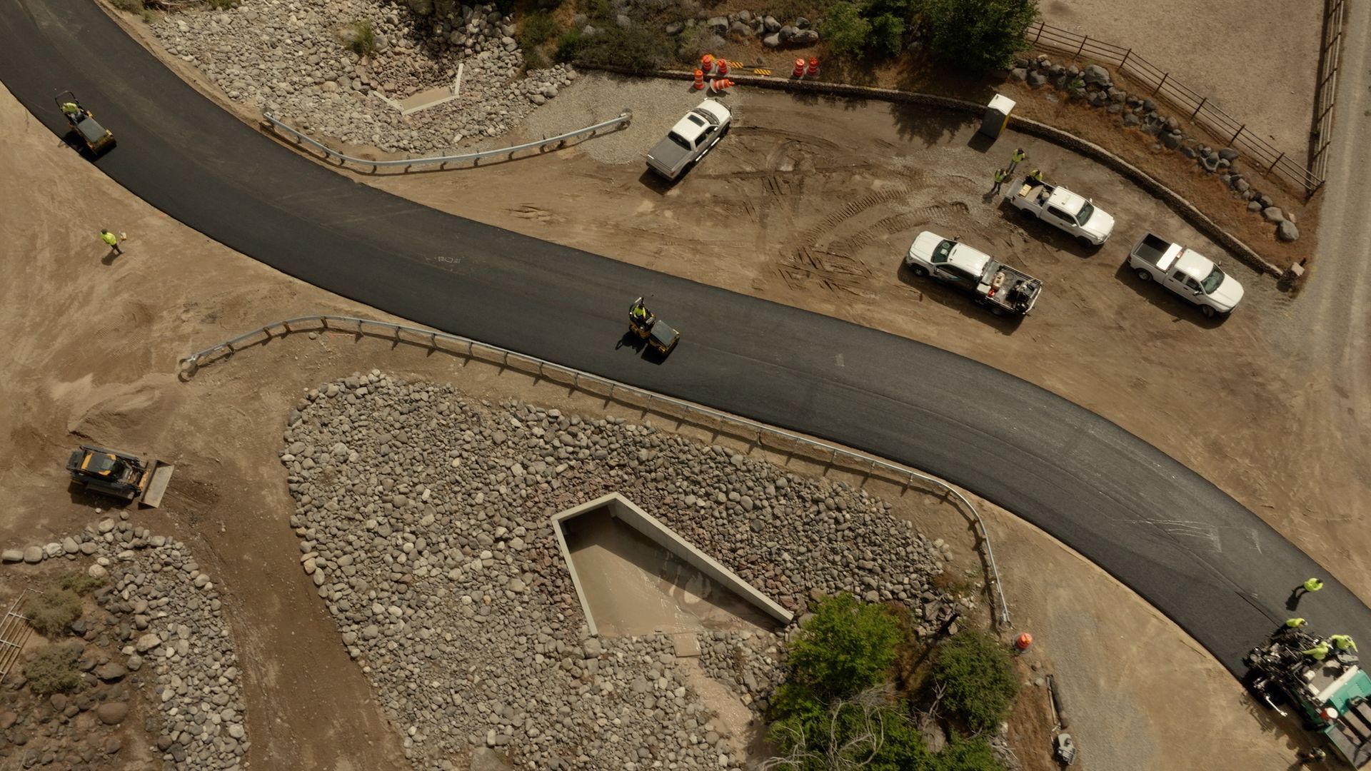 Aerial view of a winding mountain road with several parked white vehicles and a few cyclists nearby