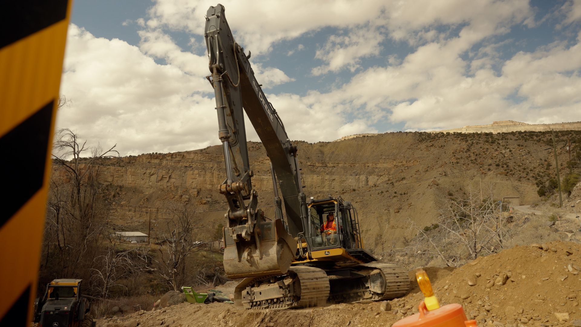 Excavator working in a rocky quarry under a cloudy sky, with a worker in the cab.