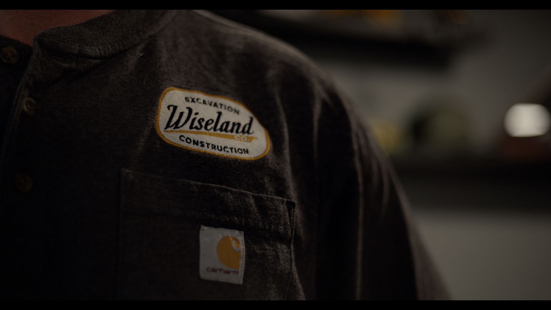Close-up of a dark jacket with a Wiseland Construction logo patch on the chest.