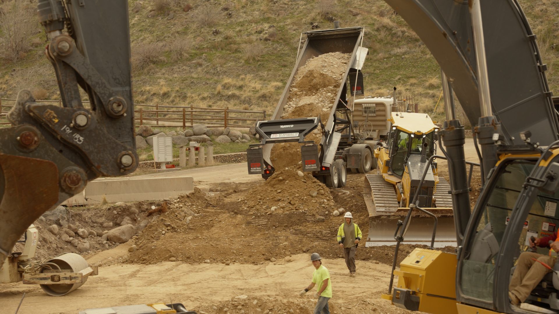 Heavy construction site with excavators, dump truck, and workers moving dirt on a road project.