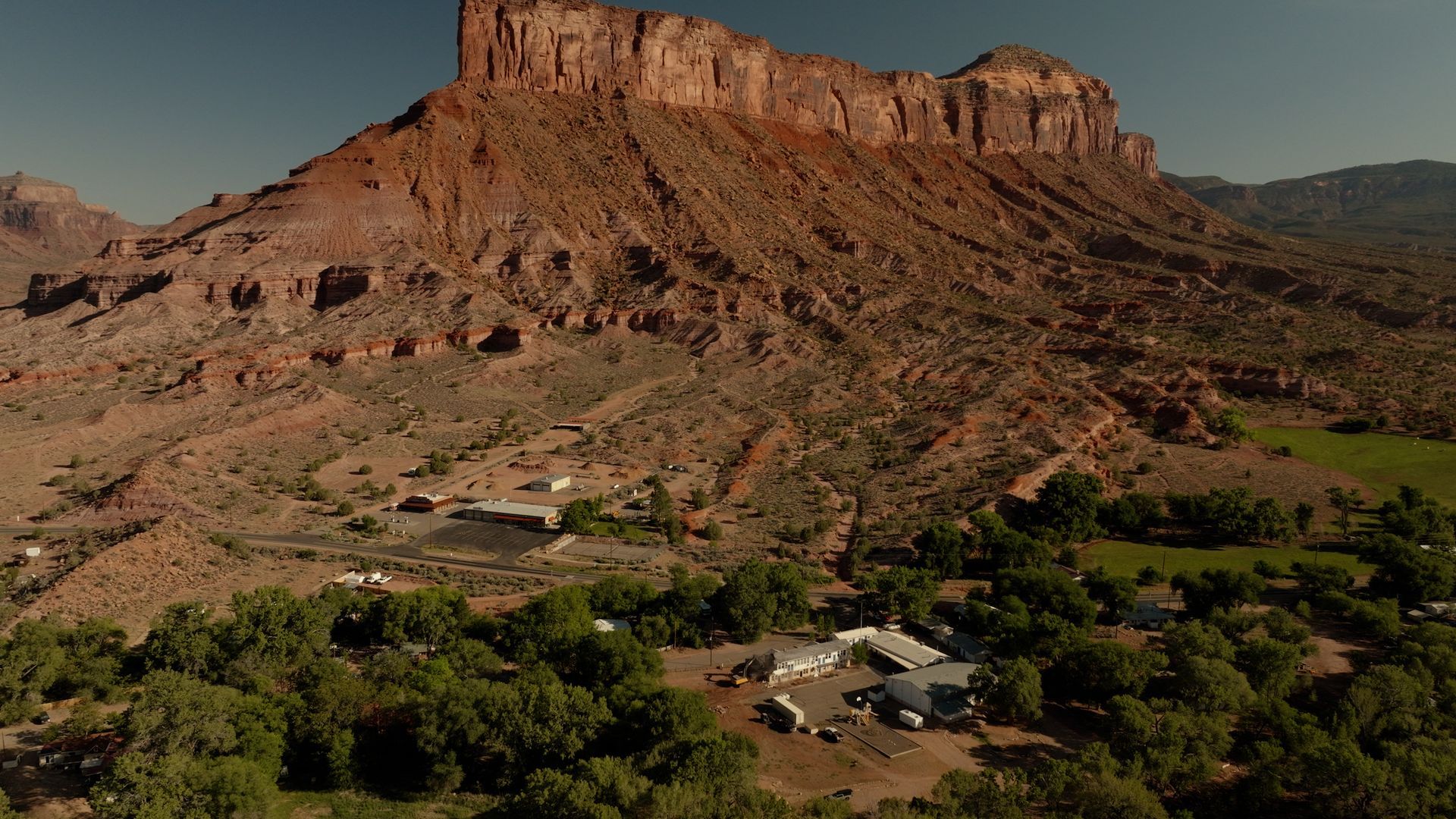 Red sandstone mesa above a green valley with scattered houses and trees under a clear sky