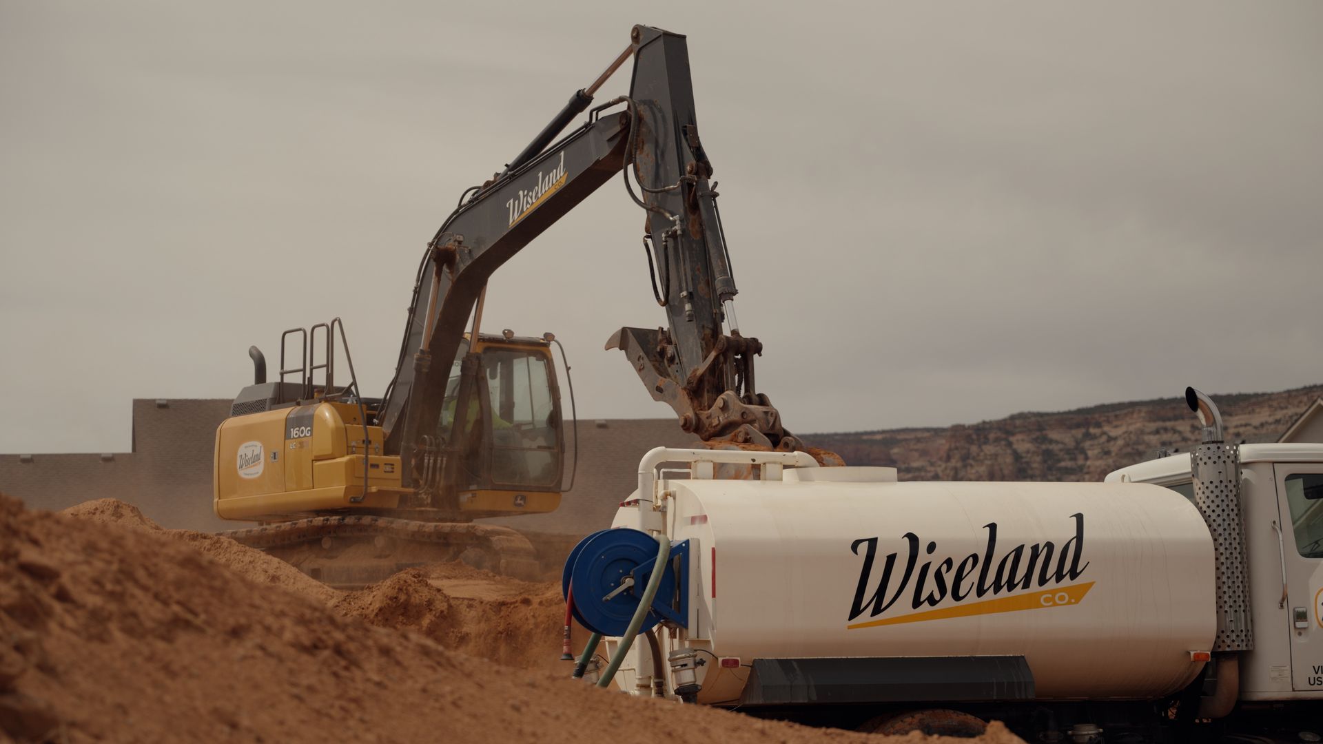 Excavator loading sand into a Wiskland truck at a dusty construction site