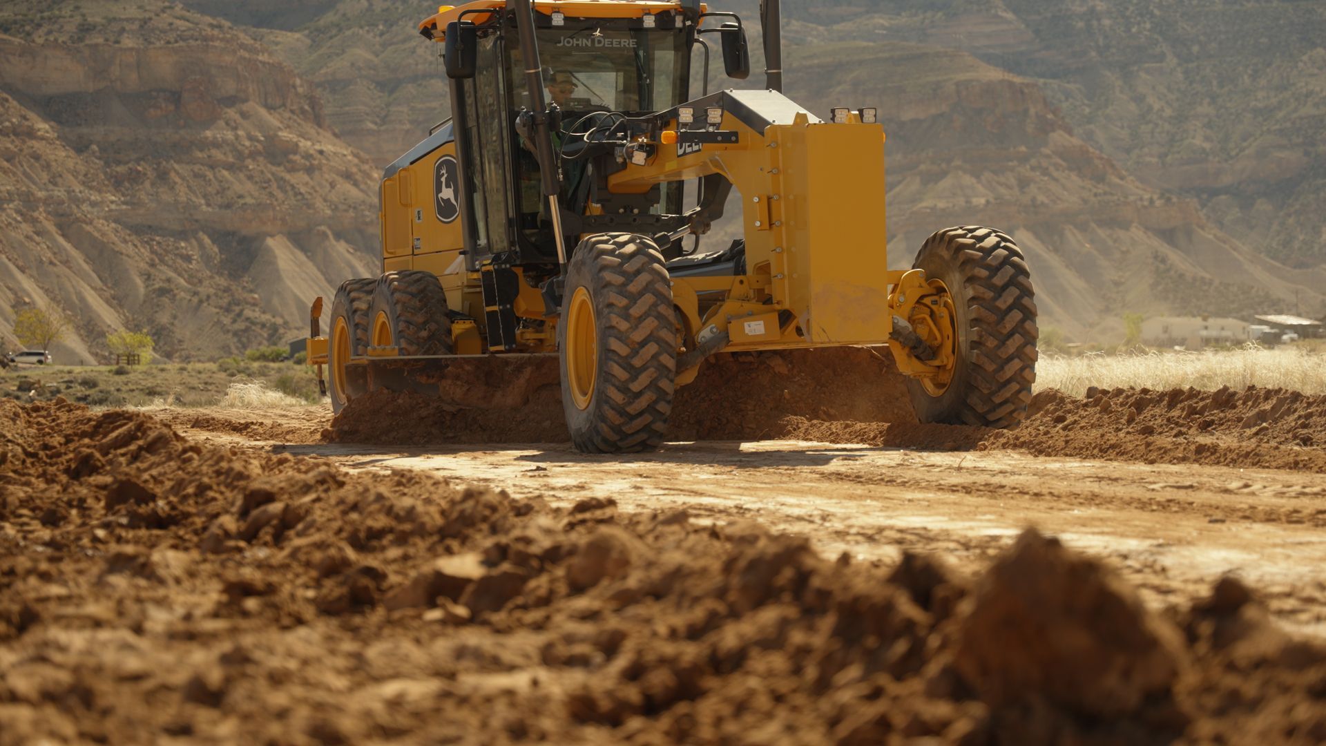 Yellow road grader working on a dusty dirt road in a rocky desert landscape