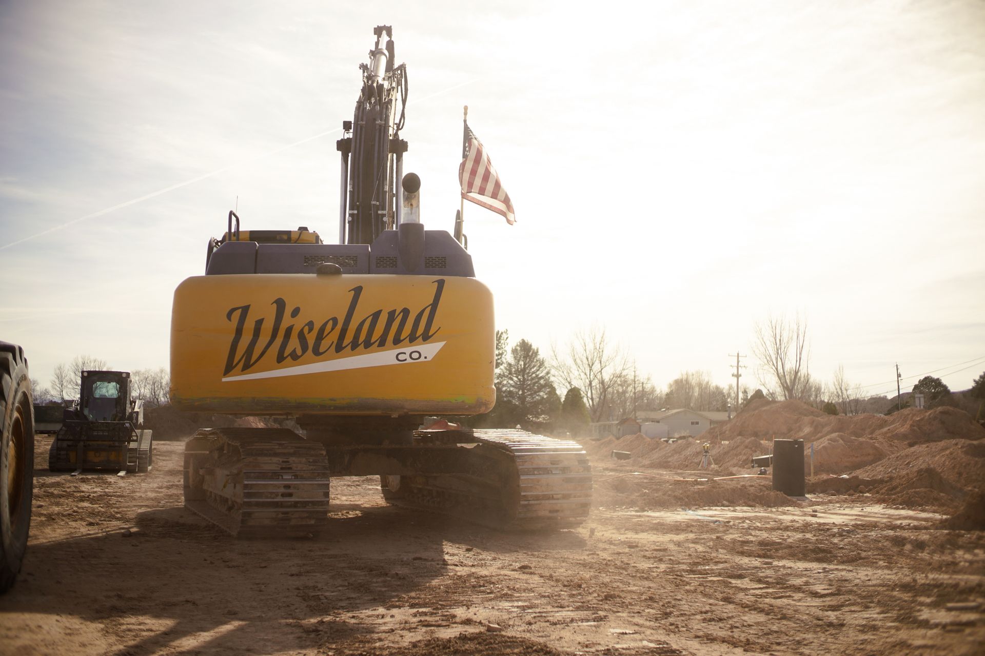 Yellow Wieseland excavator on a dusty construction site with an American flag flying in the background