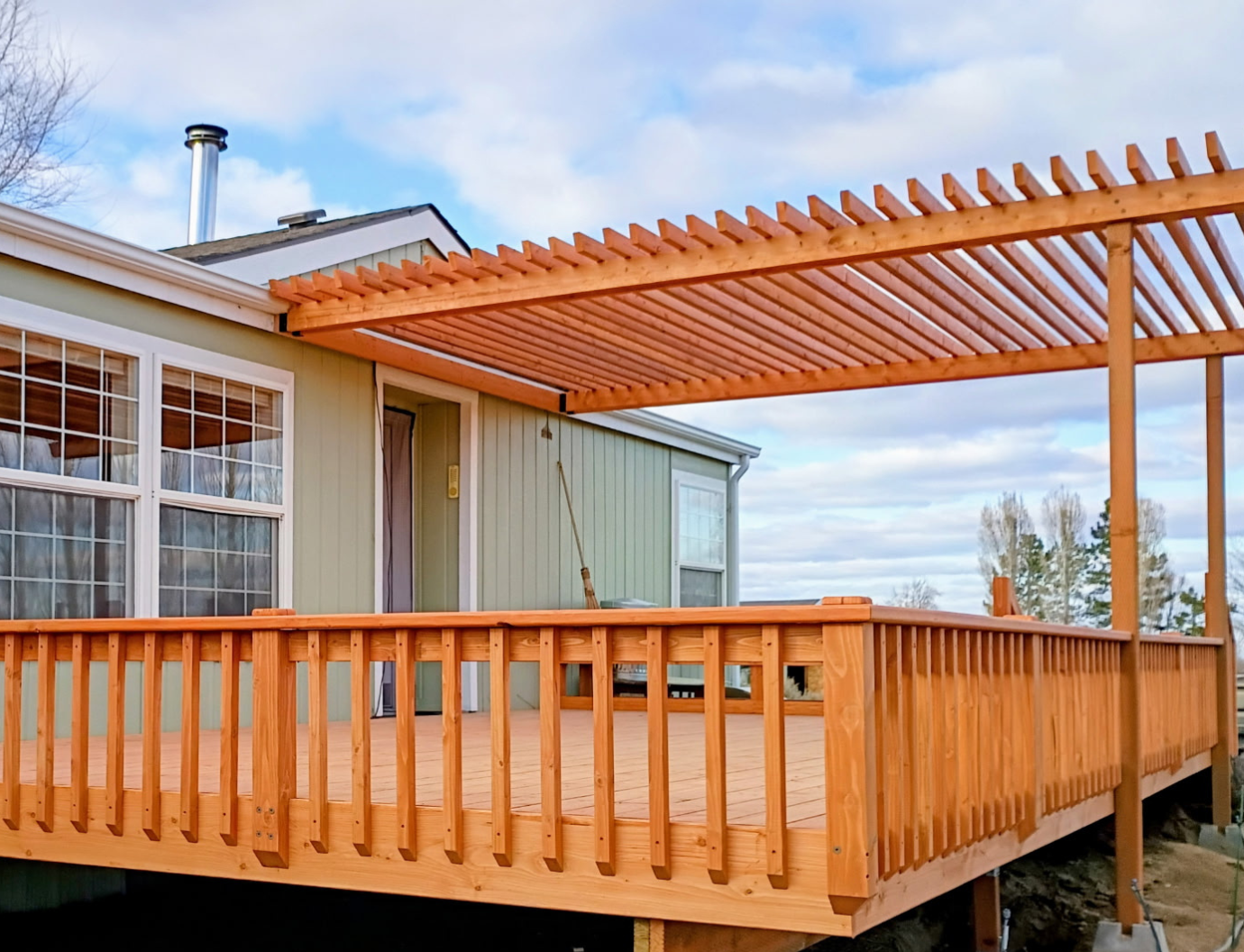 Wooden deck with orange pergola attached to a house, viewed from the backyard