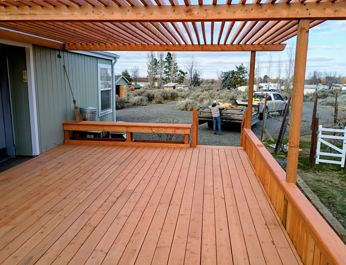 Wooden deck with pergola overlooking a rural yard and parked vehicles