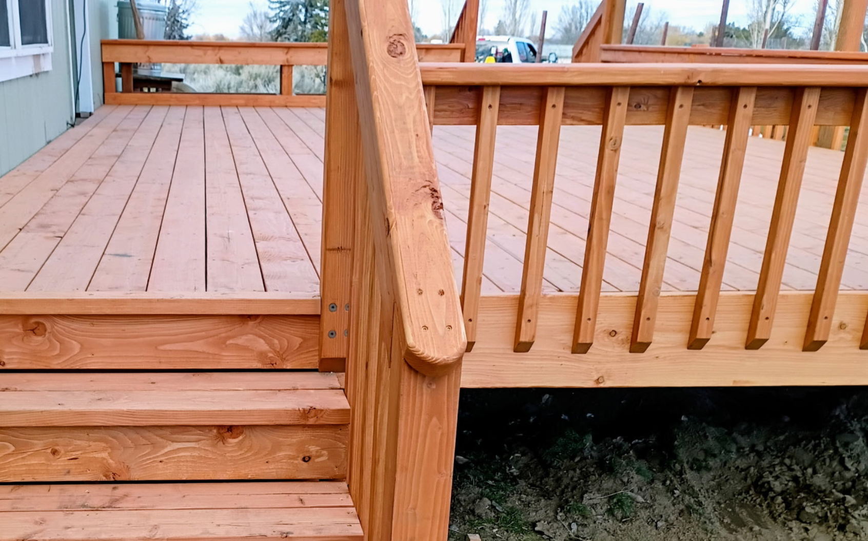 Wooden deck stairs beside a porch railing leading to a raised deck