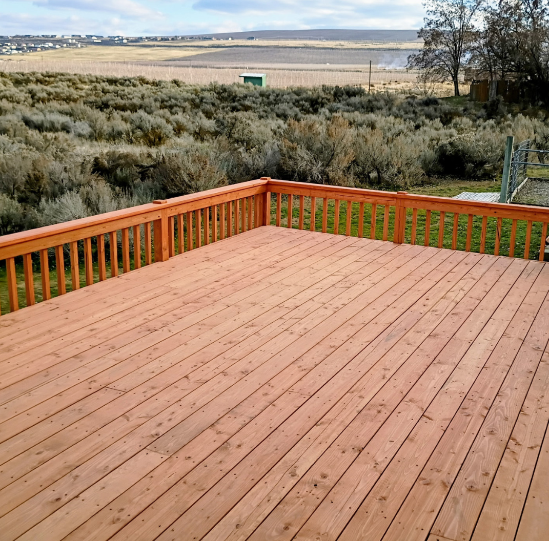 Wooden deck overlooking shrubland and open fields under a cloudy sky