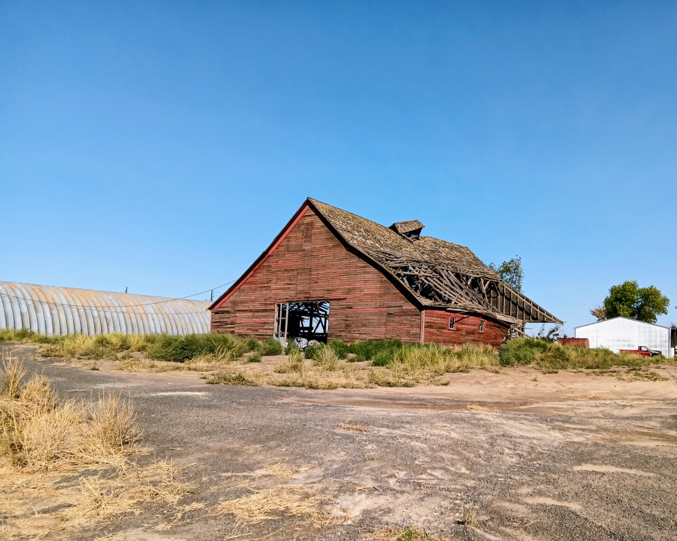 Weathered red barn in a dry field under a clear blue sky