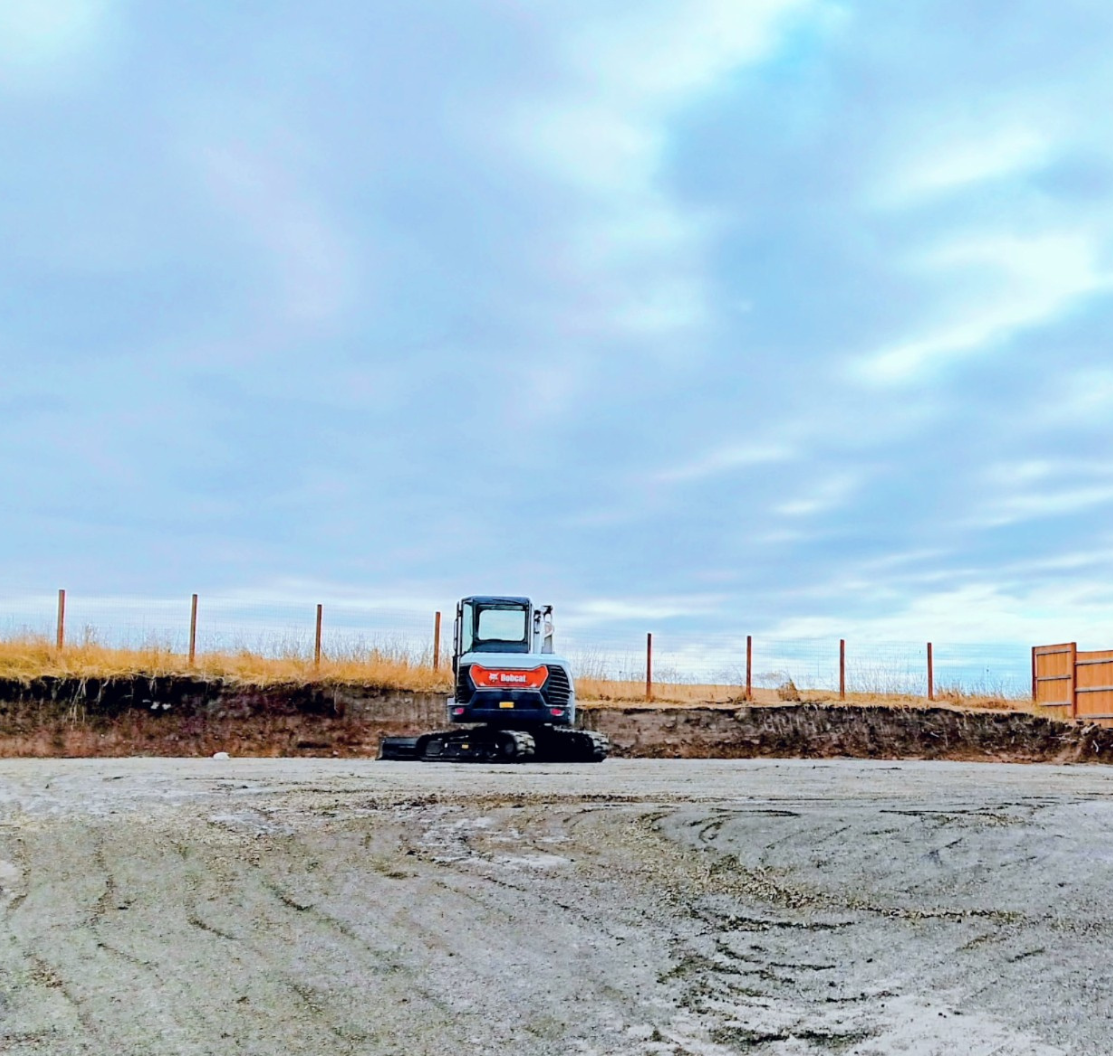Small blue tractor on a dirt road under a cloudy sky, with a fenced field in the background