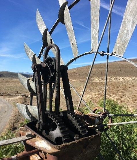 Old rusty metal machine with curved blades beside a dirt road in a dry, open landscape.