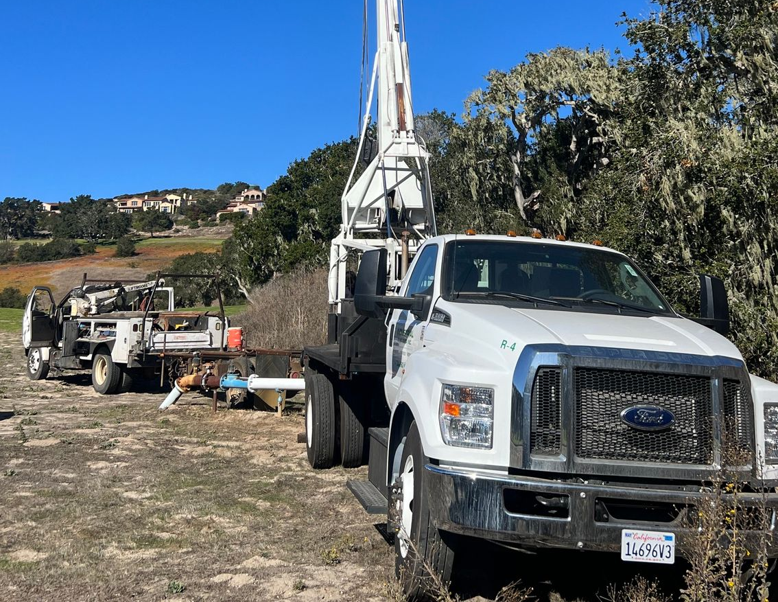 Boom truck with an extended crane parked at a rural worksite.