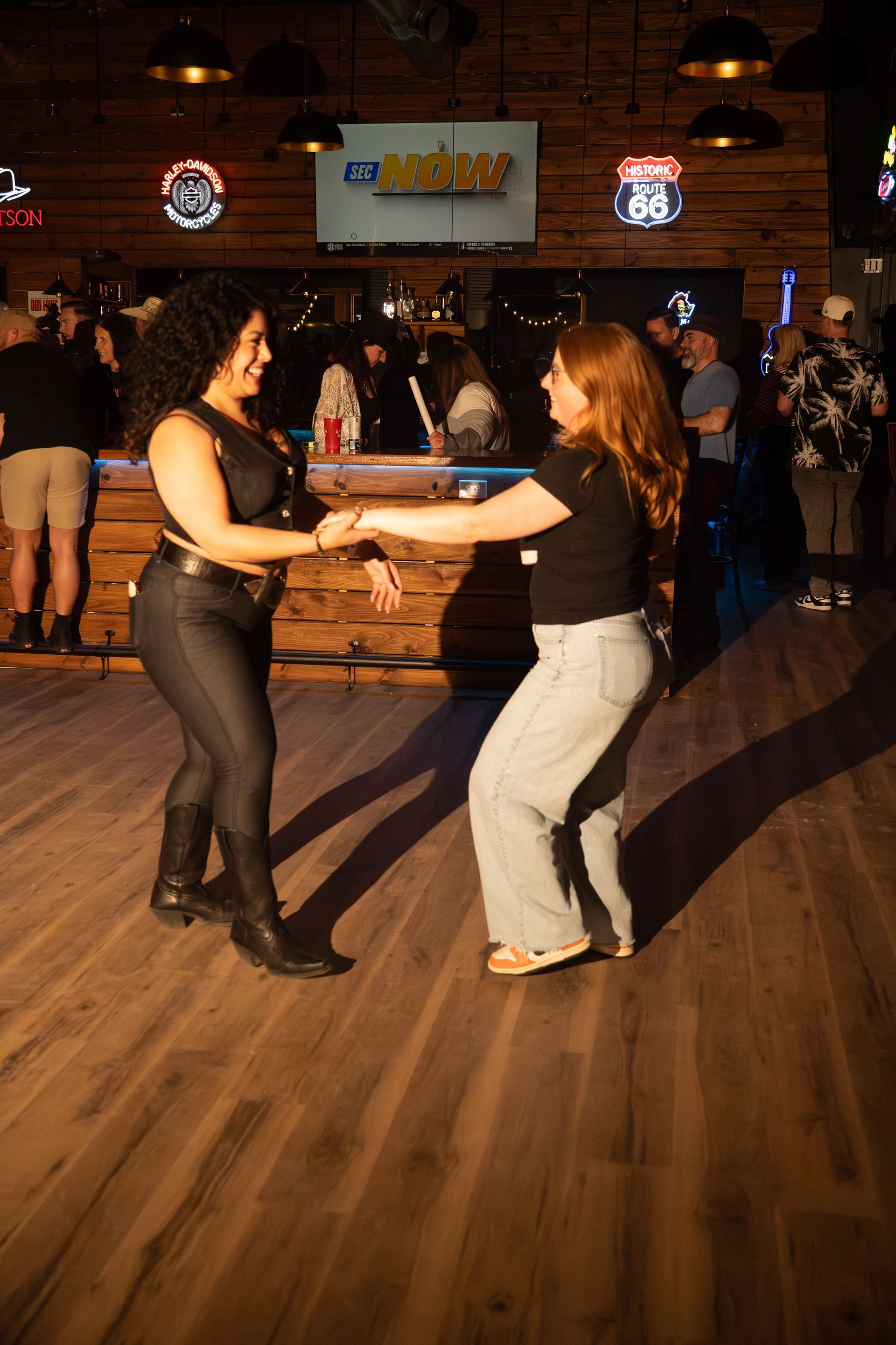 Two people dancing hand-in-hand in a dimly lit bar with a wooden floor