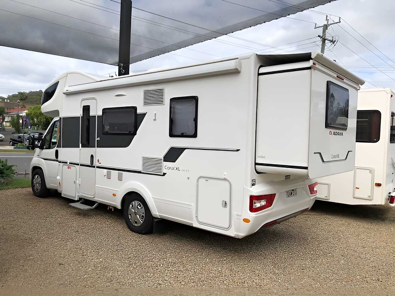 A White Motorhome Is Parked Under A Canopy In A Gravel Lot — Perkins Caravans in Byron Bay, NSW