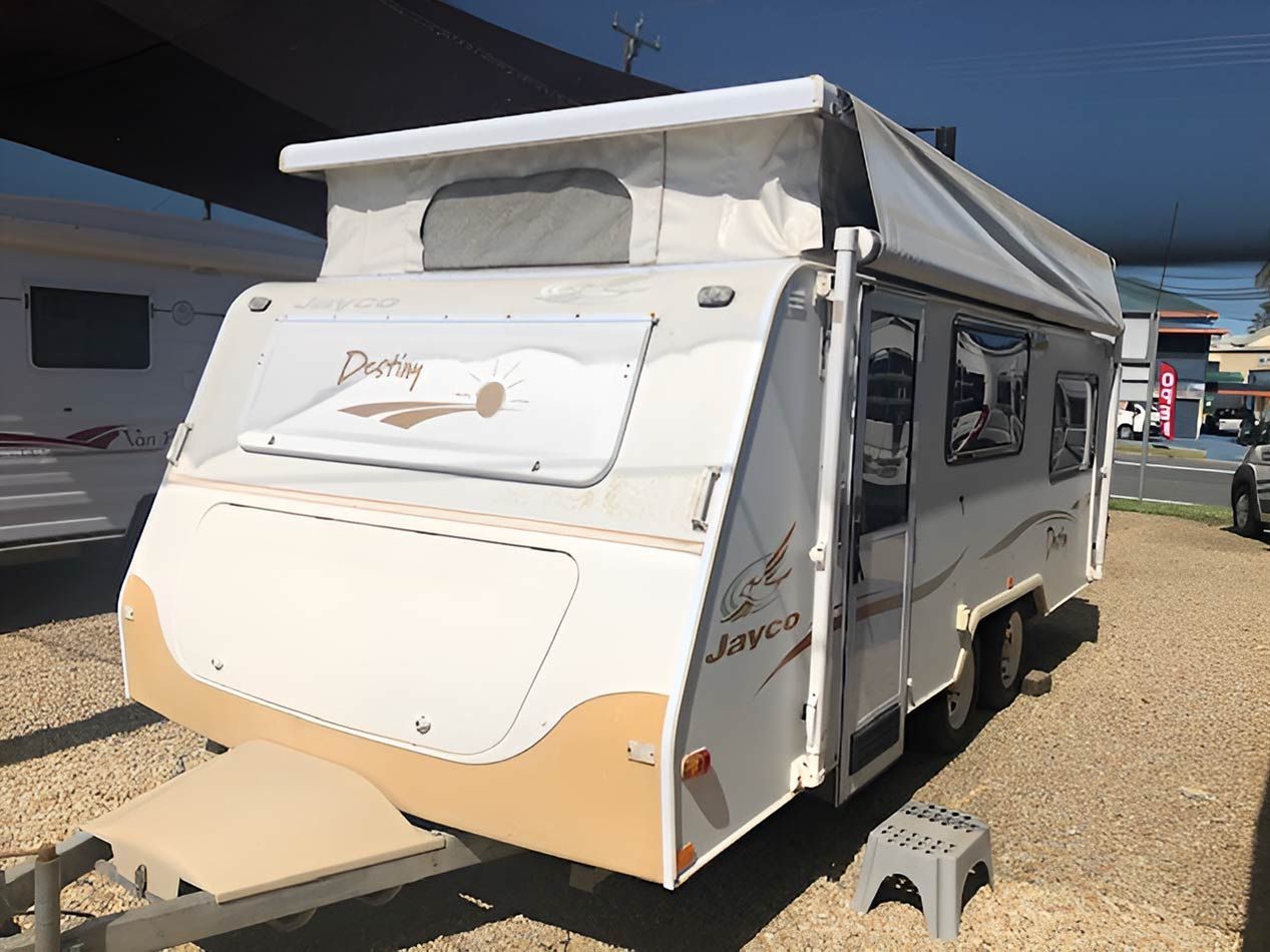 A White Camper Trailer With A Tent On Top Is Parked In A Gravel Lot — Perkins Caravans in Ballina, NSW