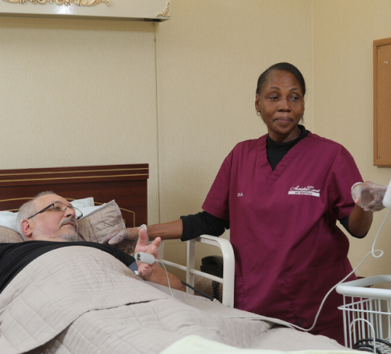 A woman in a purple scrub is standing next to a man in a hospital bed
