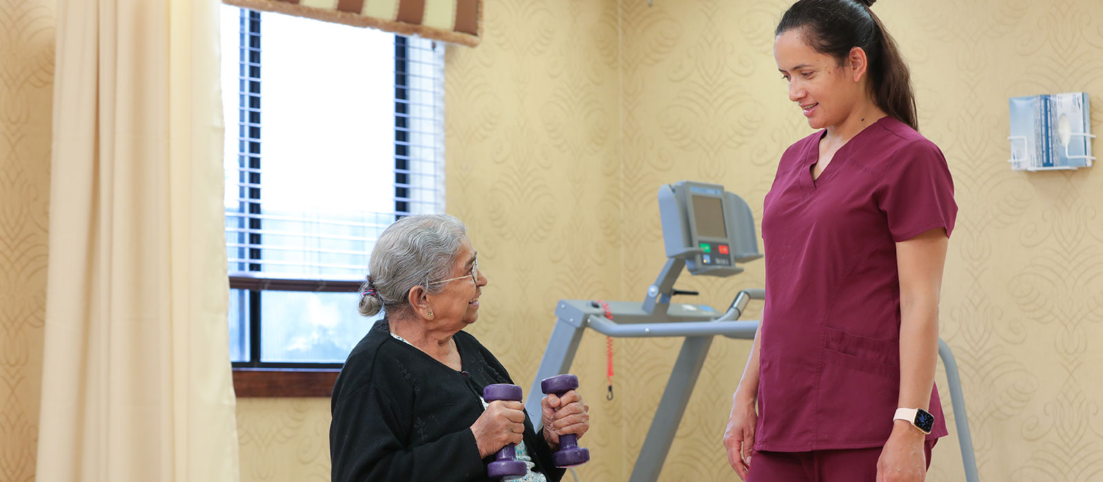 A nurse is helping an elderly woman lift dumbbells in a gym.