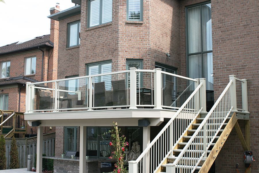 A brick house with a deck and stairs leading up to it by Premier Decks & Awnings