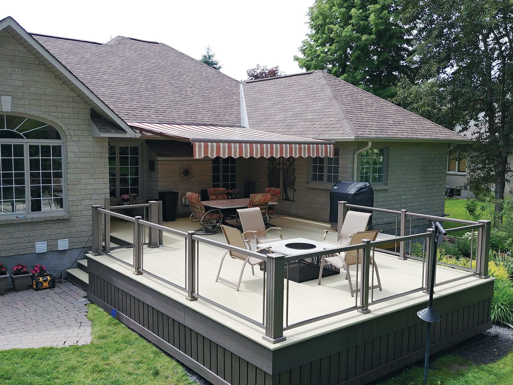 A house with a large deck with a table and chairs on it by Premier Decks & Awnings