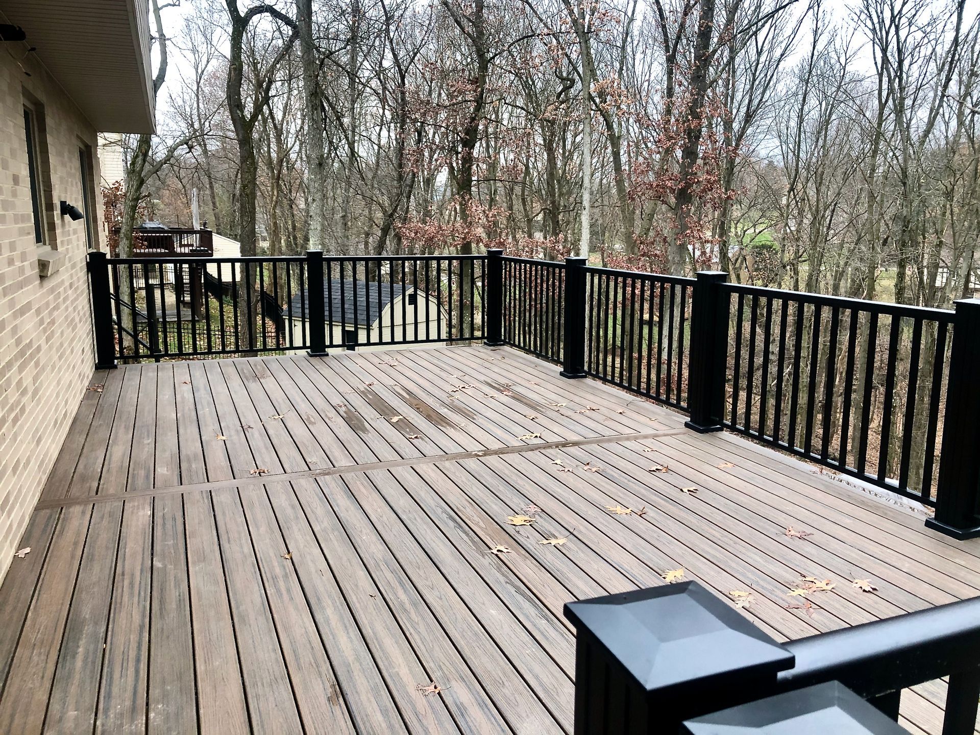 A large wooden deck with a black railing and trees in the background by Premier Decks & Awnings