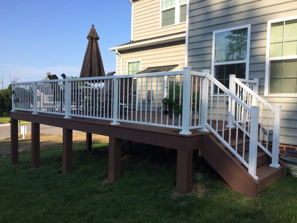 A deck with a white railing and stairs in front of a house by Premier Decks & Awnings