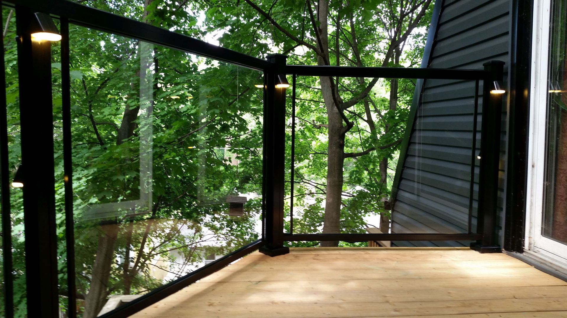 A deck with a glass railing and trees in the background by Premier Decks & Awnings