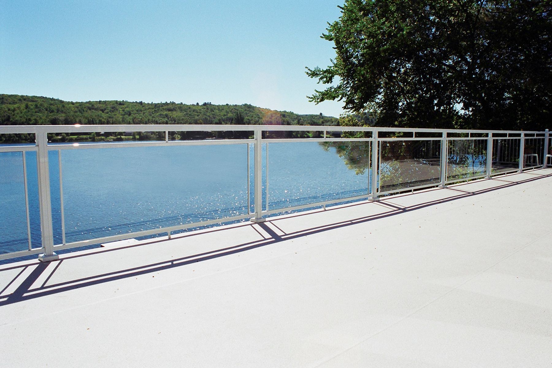 A bridge with a glass railing overlooking a body of water by Premier Decks & Awnings
